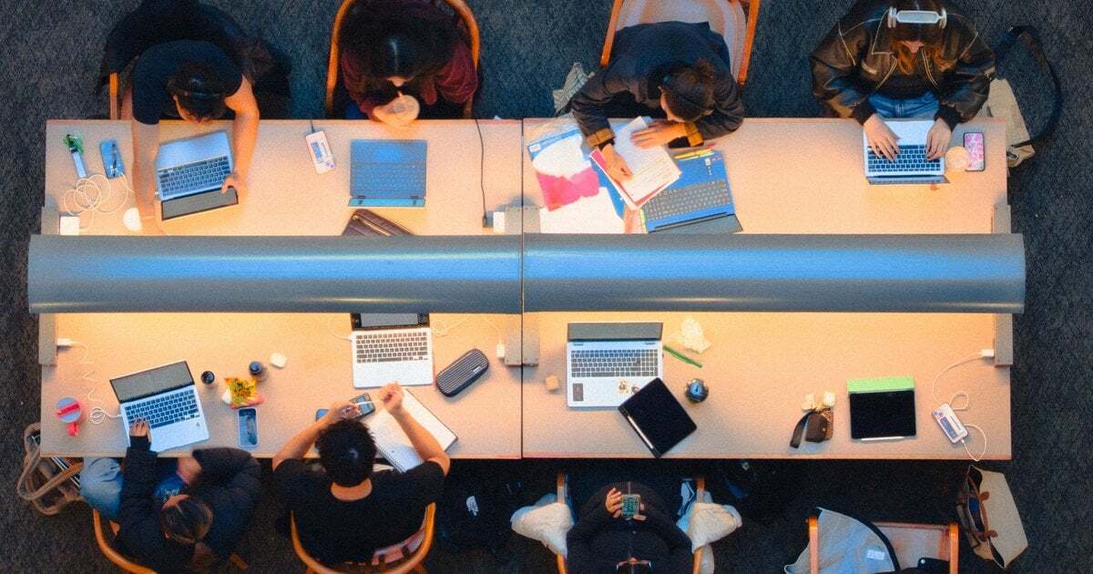 Students working on laptops at long library desks, seen from above