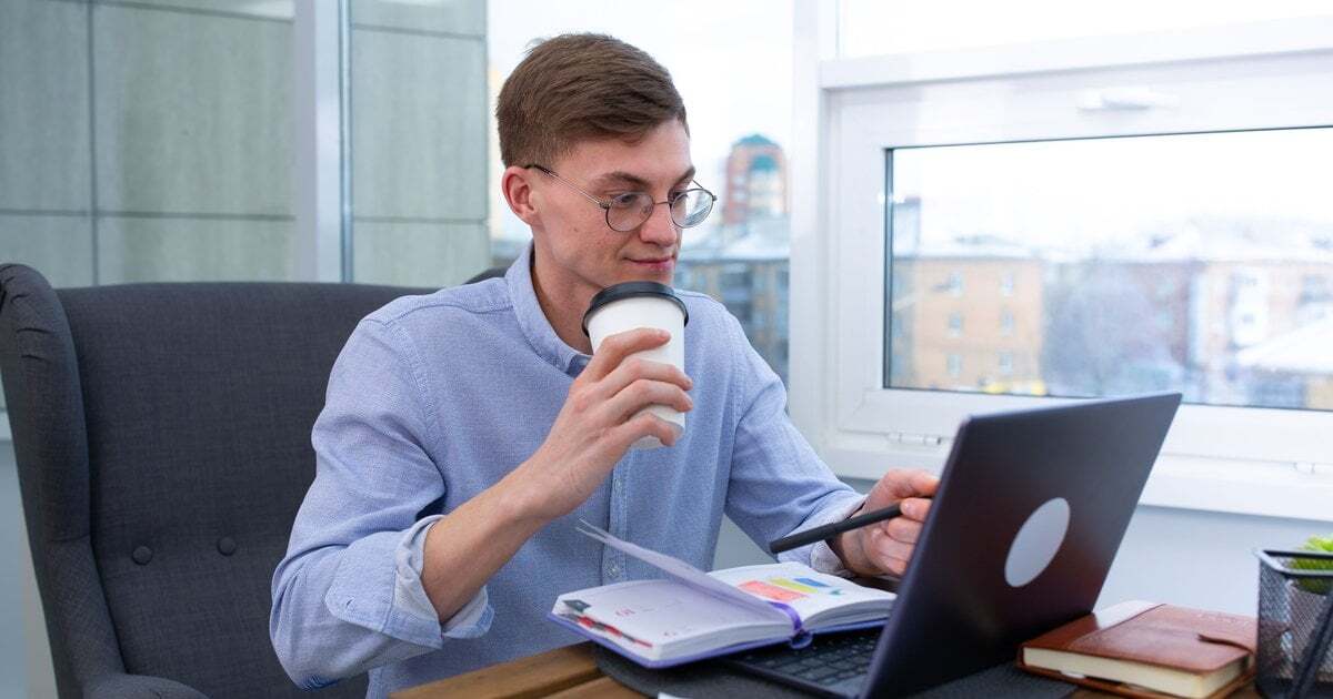 A professional with a coffee comparing options on a laptop, a planner open beside it