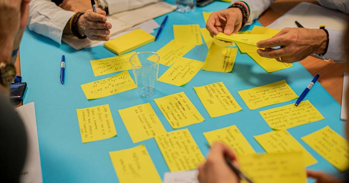 Hands arranging handwritten sticky notes across a table in a planning workshop