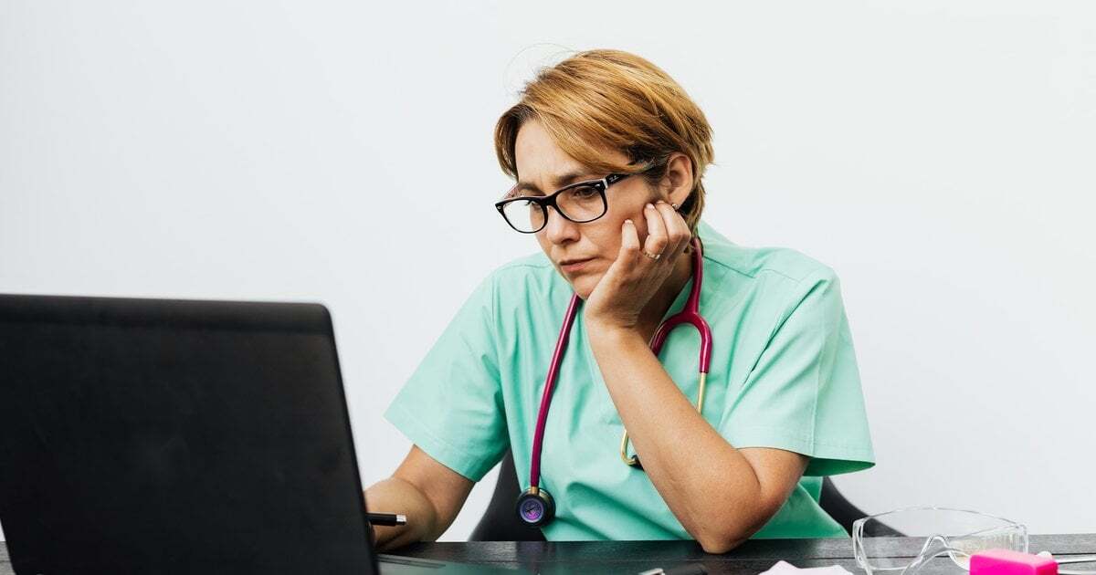 A health worker in scrubs reading guidance on a laptop