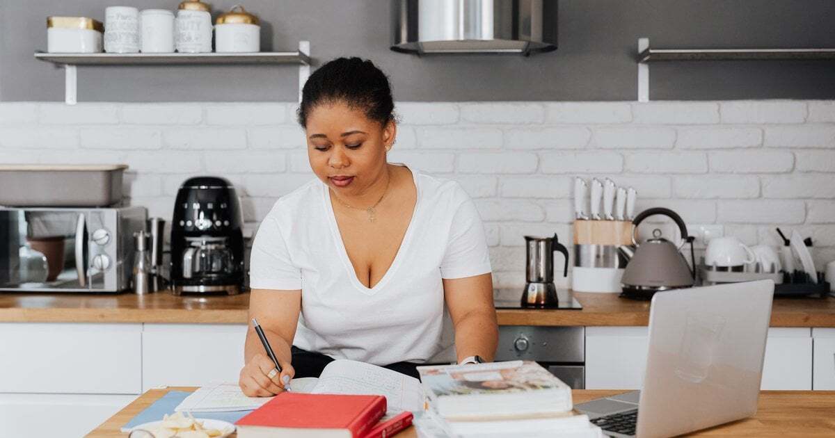 A student teacher studying with notebooks and a laptop at a kitchen bench