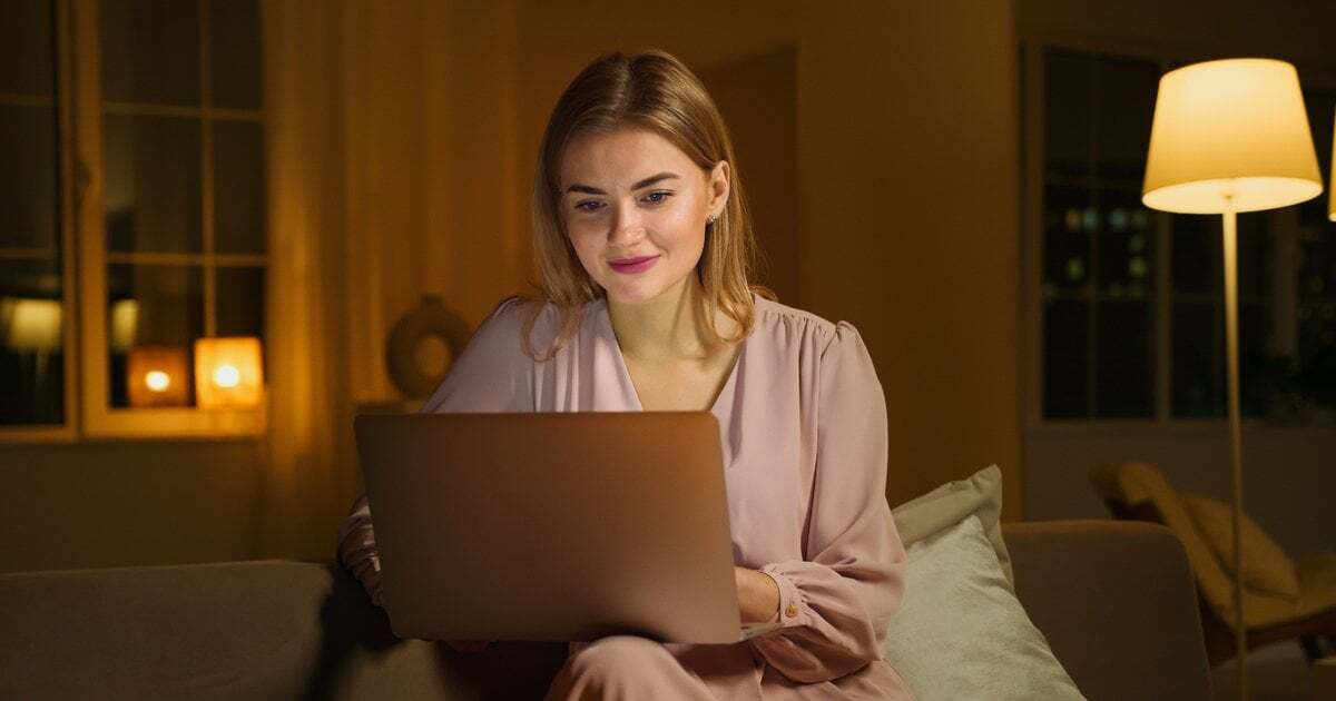 A woman studying on a laptop on her couch in the evening
